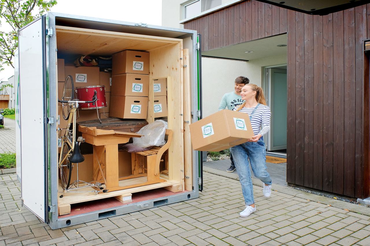 Les deux personnes de ce jeune couple sont occupées à charger la Large Box qui est prête devant leur porte.