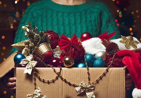 A woman carries a cardboard box full of Christmas decorations