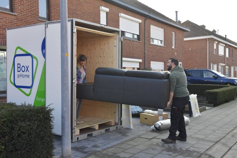 Jong koppel plaatst voorzichtig hun sofa in de Large Box die voor hun deur staat