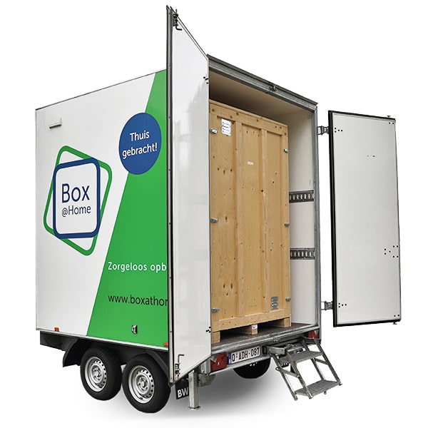 Une Large Box de Box@Home sur une remorque avec des portes ouvertes et une boîte en bois fermée.