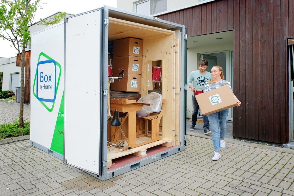 Les deux personnes de ce jeune couple sont occupées à charger la Large Box qui est prête devant leur porte.