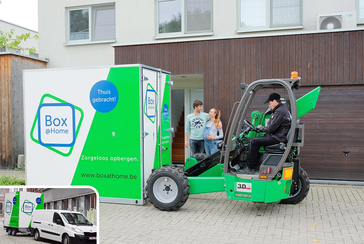 Les deux personnes de ce jeune couple ont l'air heureuses tandis que l'employé de Box@Home dépose leur Large Box devant leur porte.