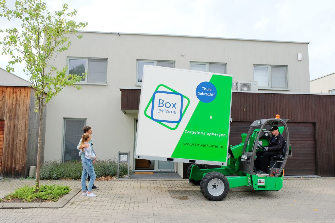 Jong koppel kijkt toe hoe de Box@Home chauffeur de Box met zijn heftruck voor hun deur plaatst