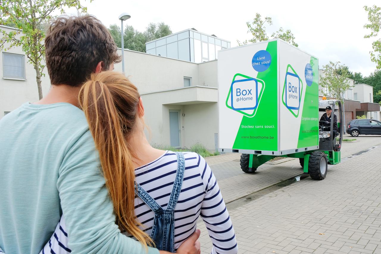 Les deux personnes de ce jeune couple sont en train de regarder pendant que le conducteur de Box@Home vient leur apporter leur boîte.