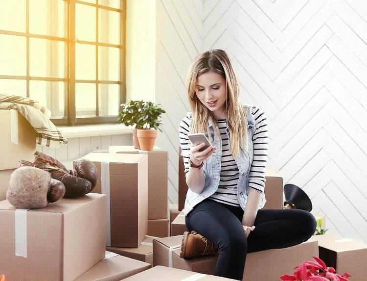 A student sits on a stack of removal boxes and orders her storage space online from Box@Home